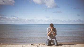 Hombre tirado en la arena de una playa que está llorando